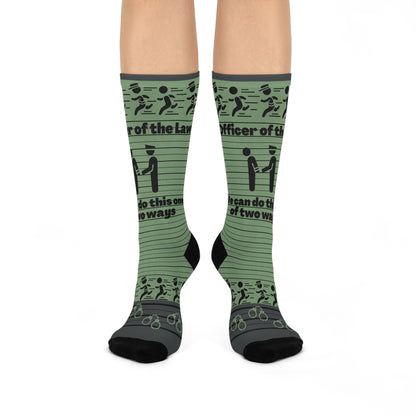 A pair of green crew socks with text and graphic patterns related to law enforcement, including phrases such as 'Law and Order' and 'Officer of the People'.