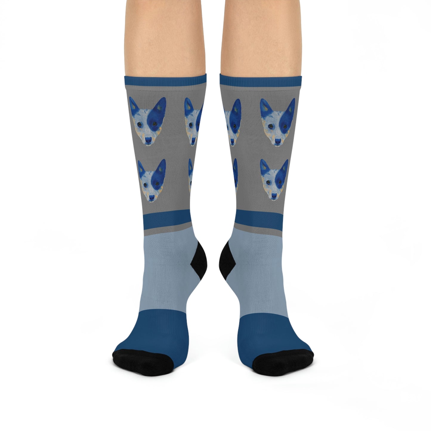 A pair of blue and gray mid-calf socks with a design of two blue healer dogs and a part of a human foot visible.